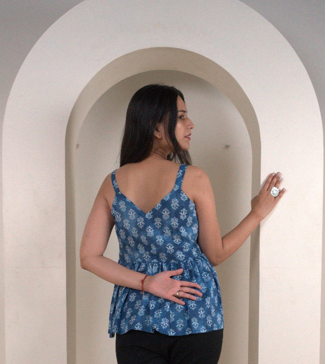 Woman in a blue patterned top and black pants standing on a white platform with a neutral background